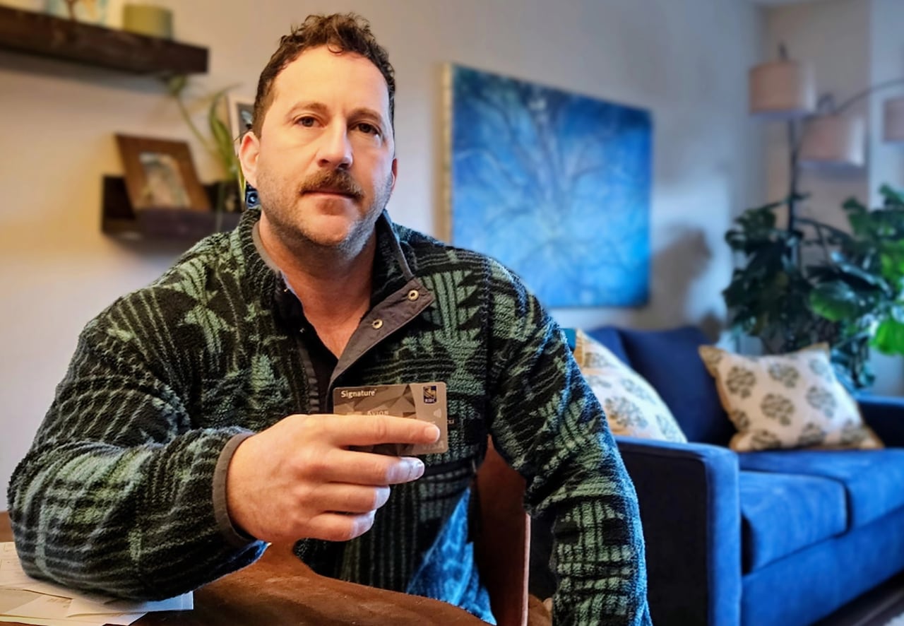 Man seated at table, looking at camera and holding a bank card in one hand