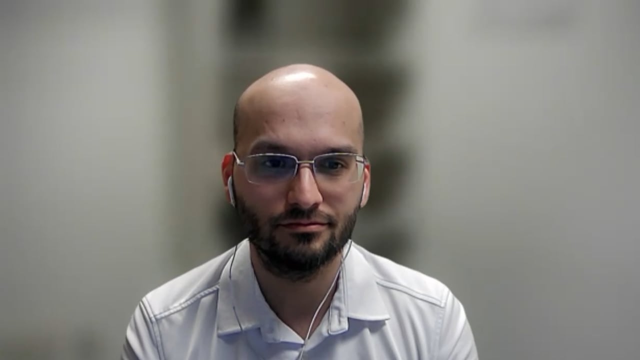 Bald man with beard and eyeglasses wears a white collared shirt. 