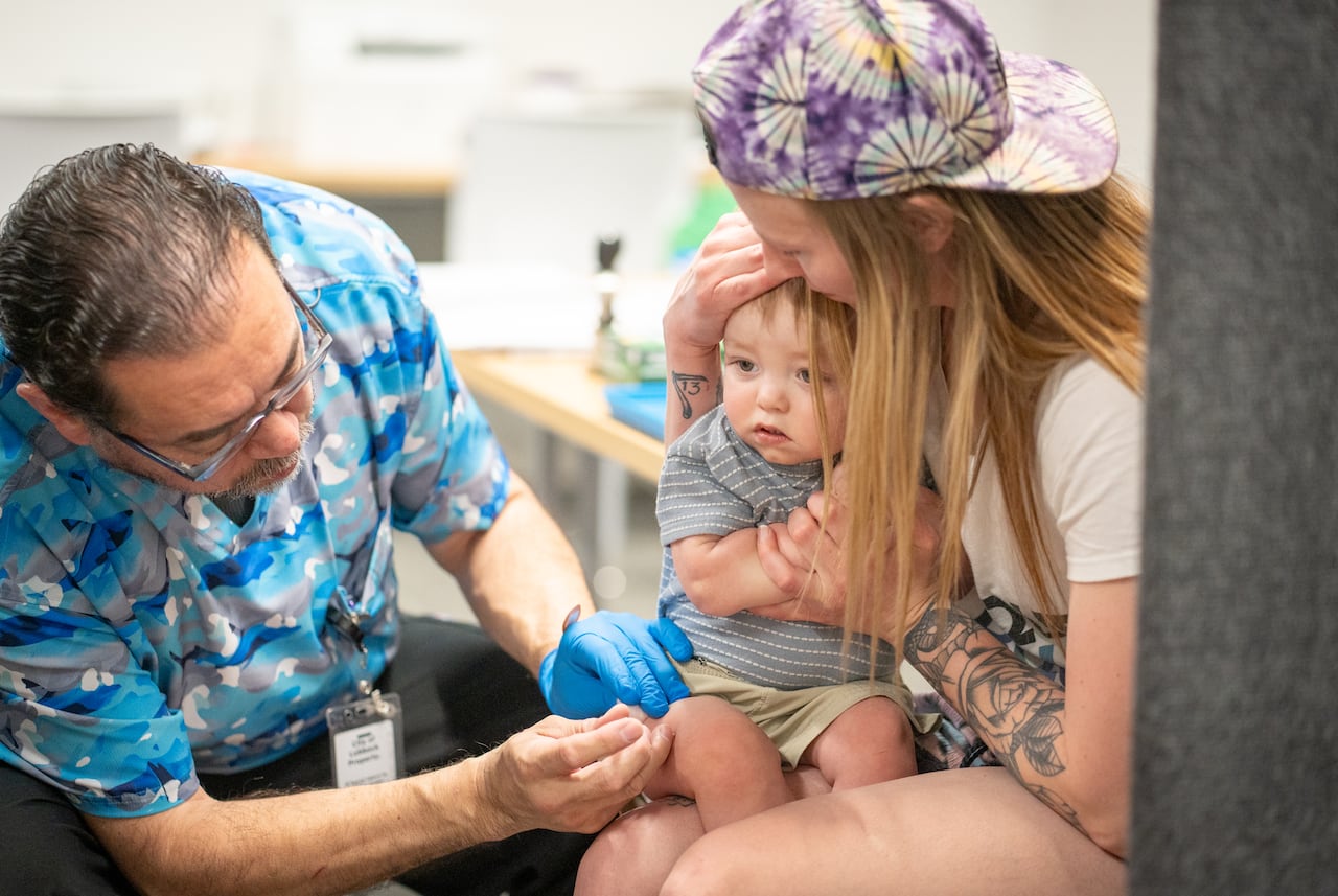 A one-year-old is held by his mother while he receives an MMR vaccine.