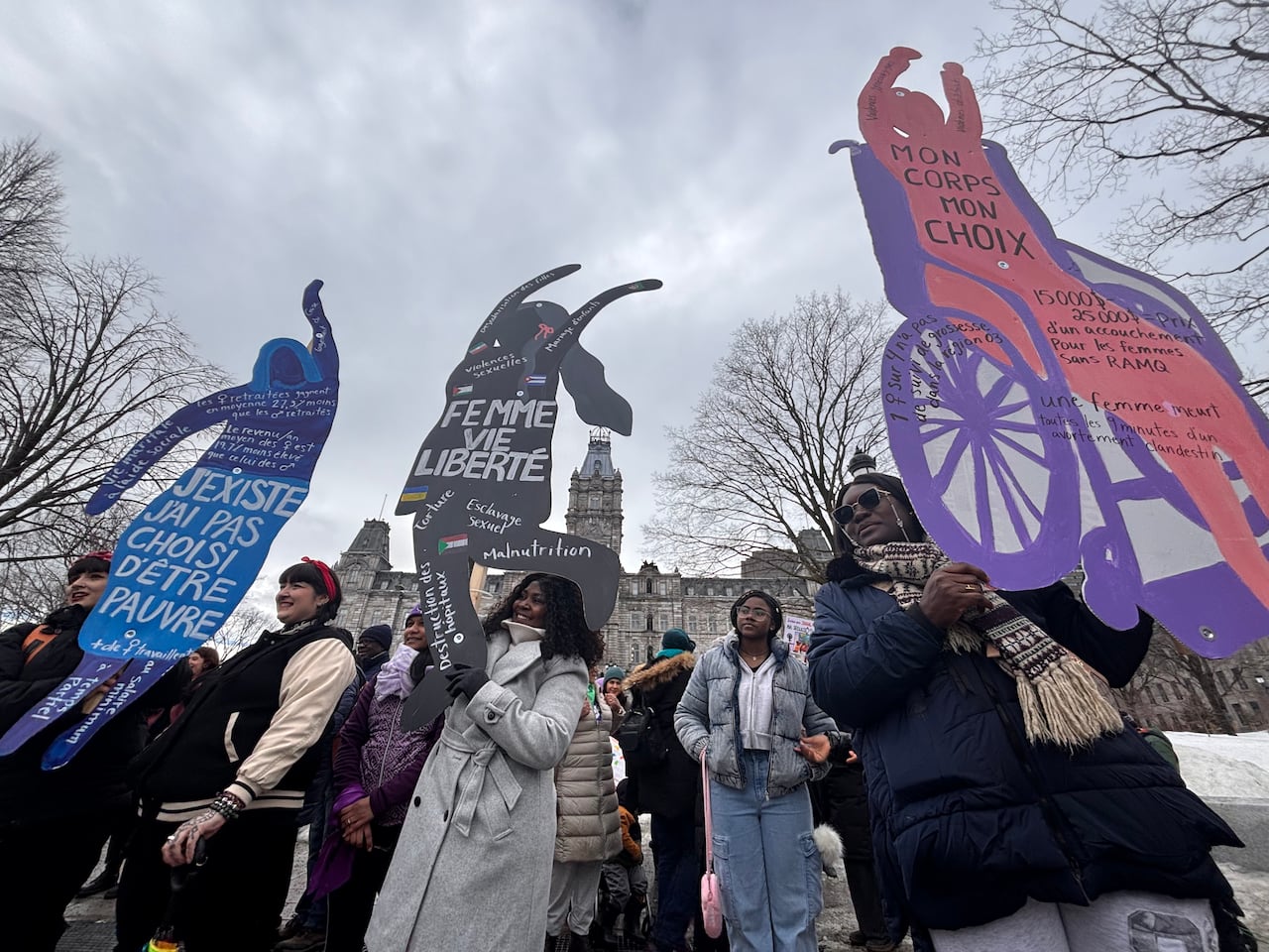 Women stand outdoors holding signs.