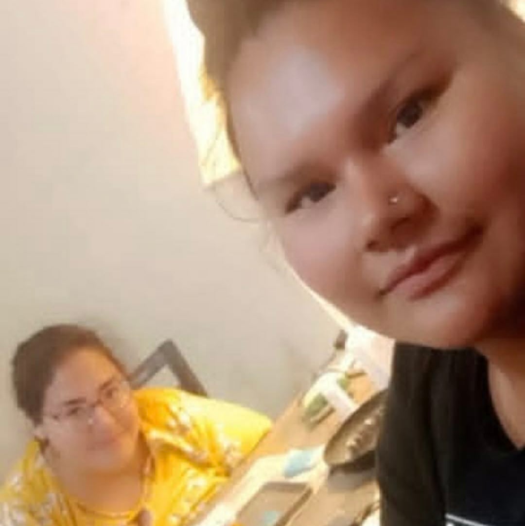 A woman wearing a yellow floral shirt smiles as she sits across from a woman in a black shirt.