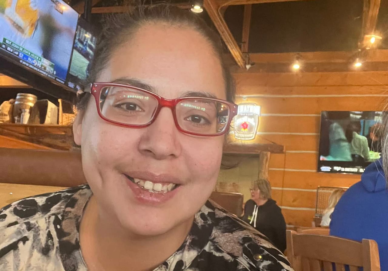 A woman wearing glasses and a leopard print shirt sits and smiles. 
