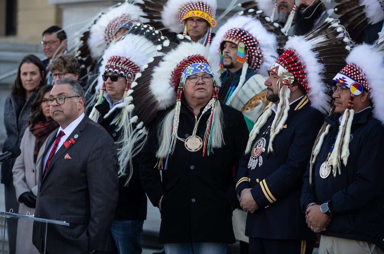 Men in suits and indigenous headdresses stand shoulder to shoulder