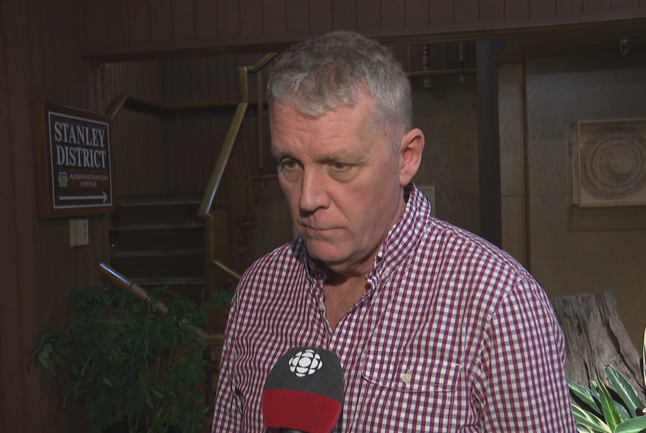 A man in a checked shirt speaks in a wooden reception area.