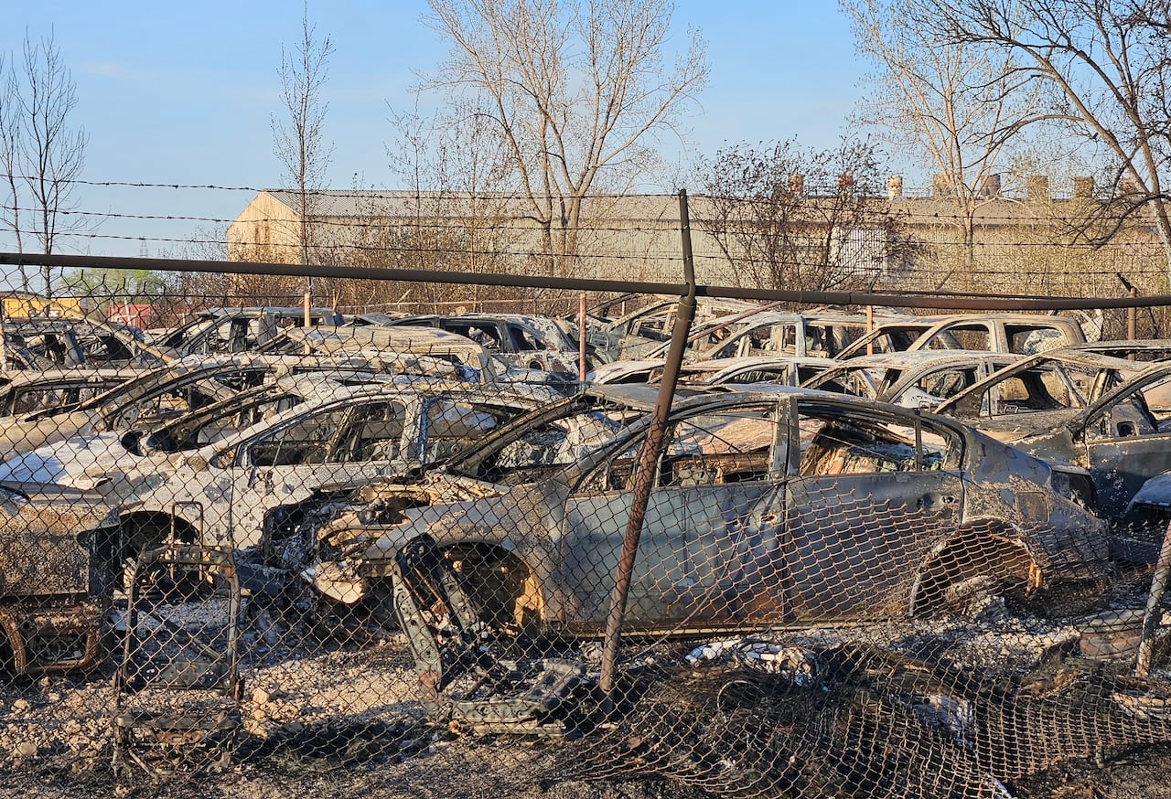 An auto parts yard is seen through a chain link fence with burned vehicles.