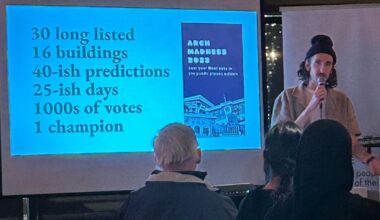 A man speaking to an audience next to a slide about Arch Madness.