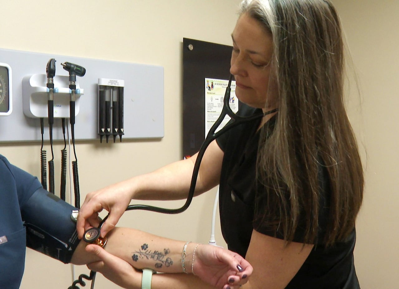A woman wearing doctor's scrubs holds a stethoscope to the arm of a patient.