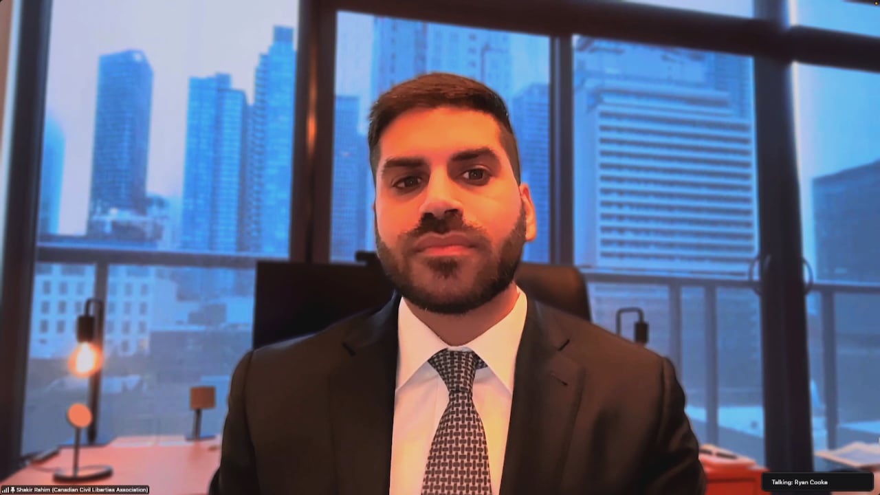A man in a suit sitting in front of a window with a city view.