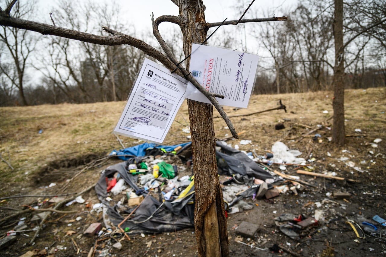 Encampment clear-out notices placed on a tree with lots of garbage behind it
