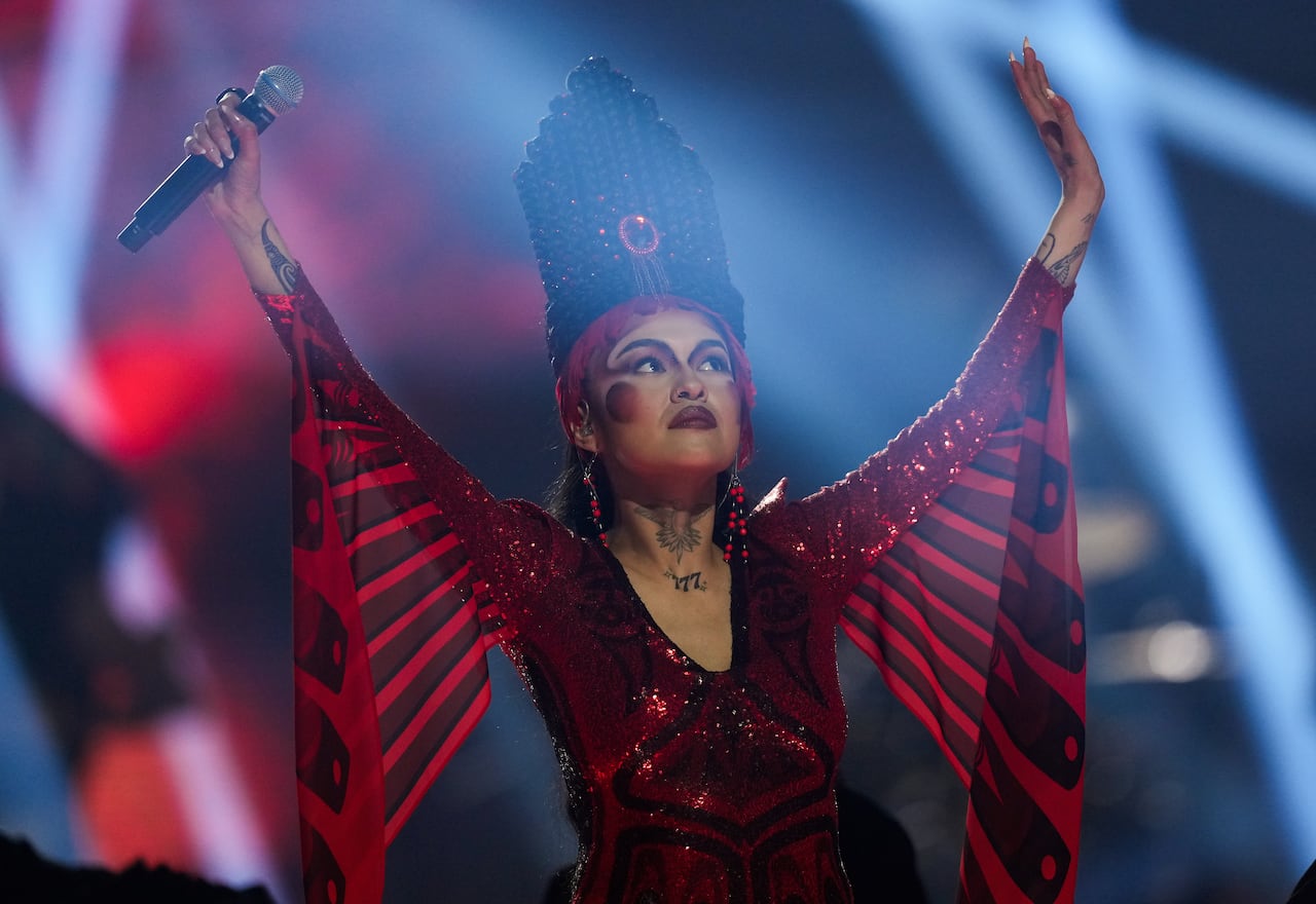 A performer in red flowing clothing and a tall headwear holds her arms up