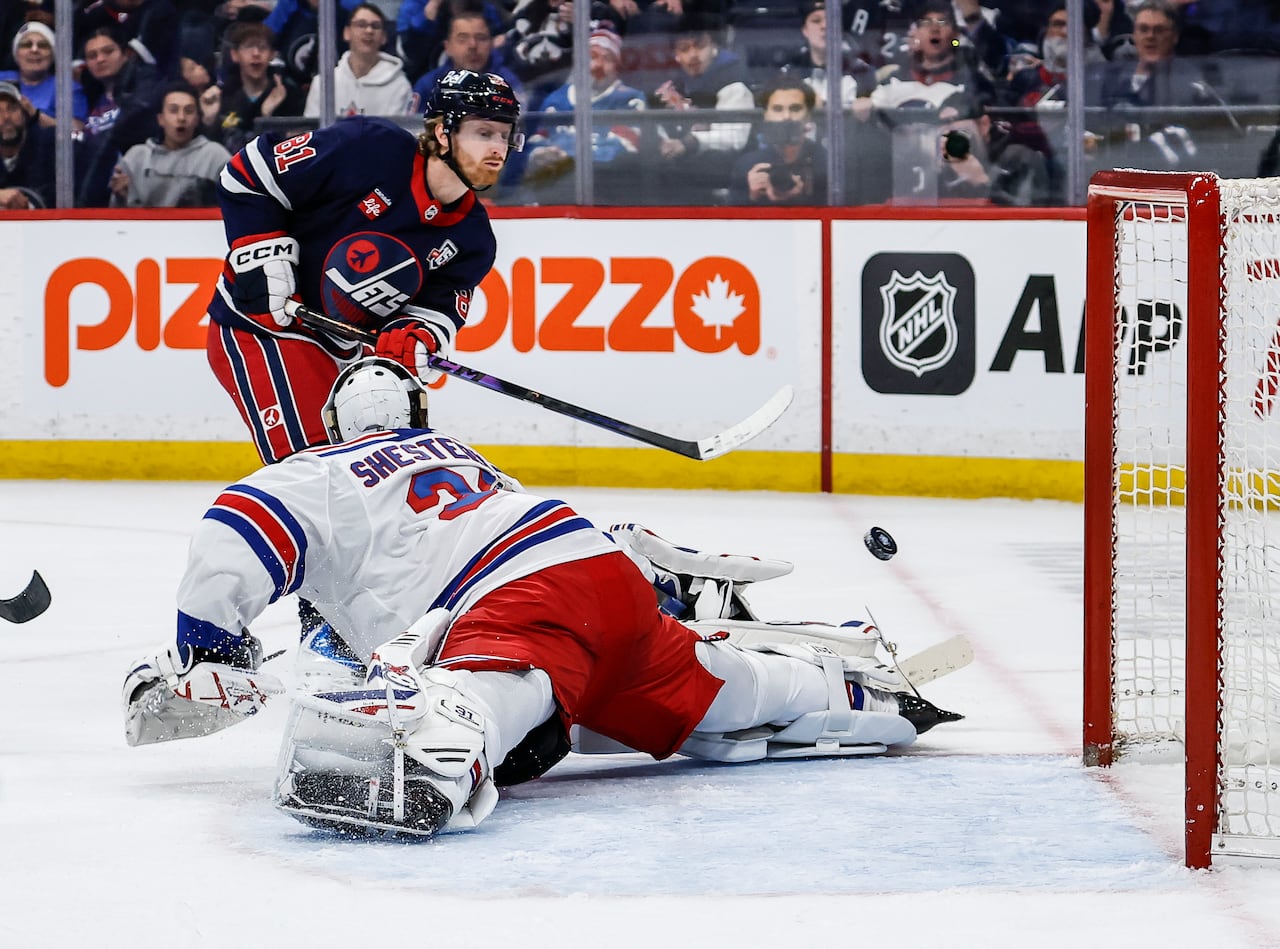 A Jets player lifts the puck past the sprawling Rangers goalie.