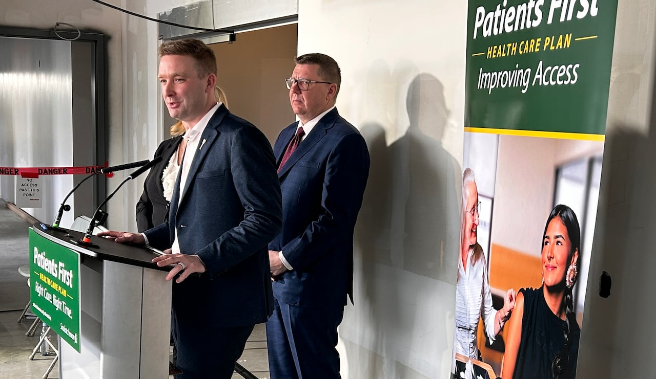 A man speaks at a white lecturn in a room with white walls