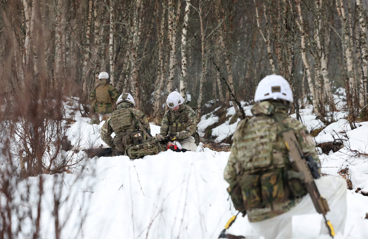 Four soldiers wearing winter camoflage crouch in a forest