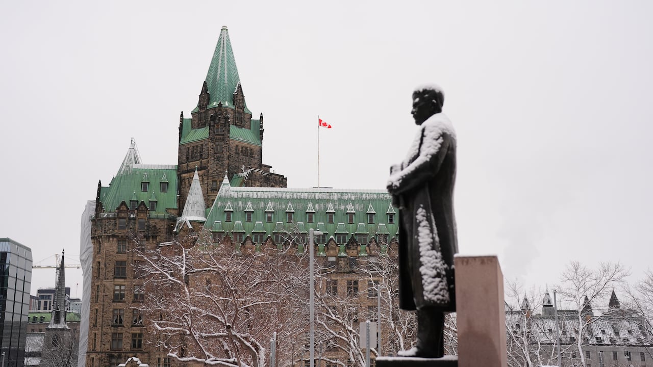 A statue is covered in snow. An old brick building is seen in the background.