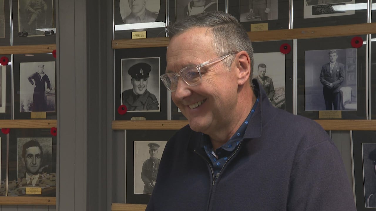 Man in glasses, blue sweater, and smiling.