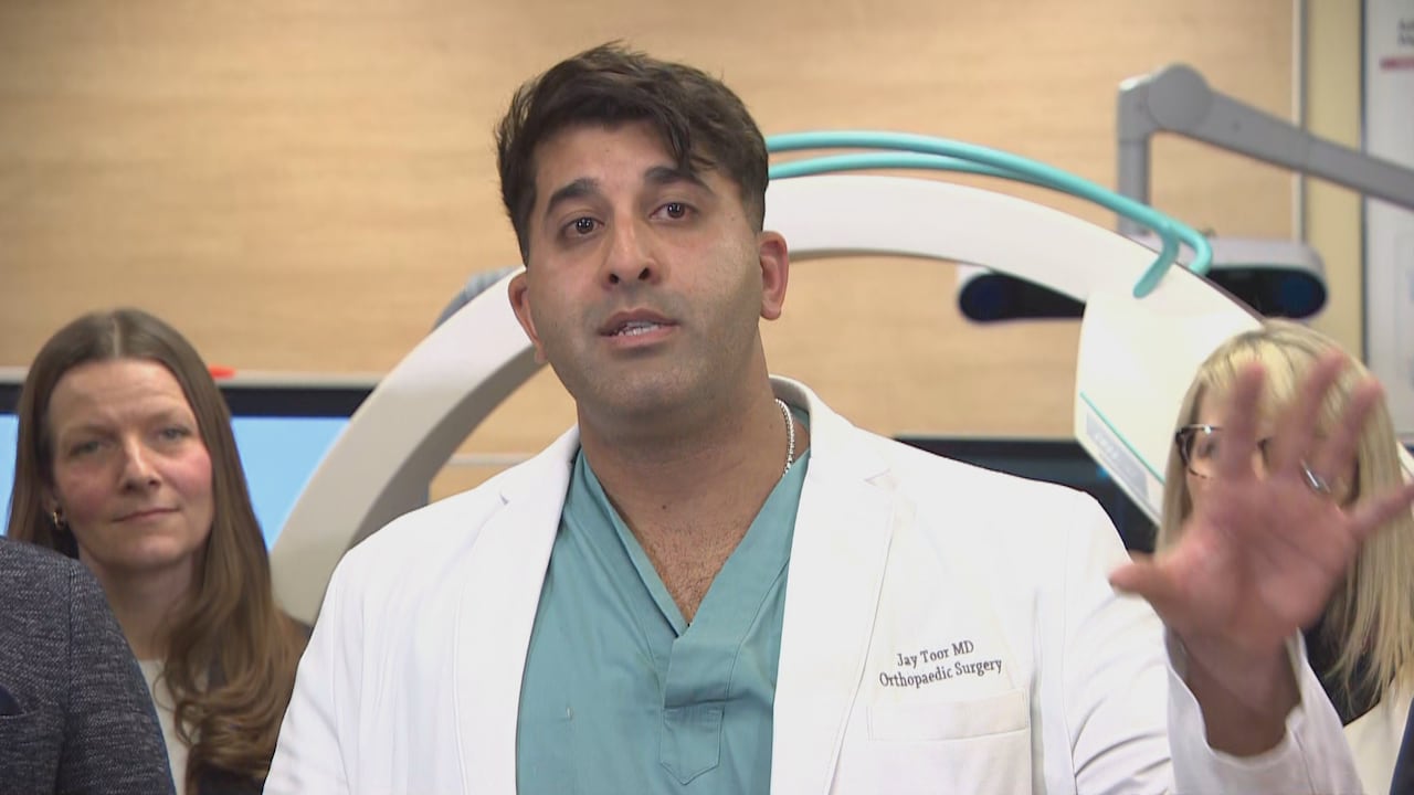 A doctor in scrubs and a whitecoat speaks during a funding announcement.