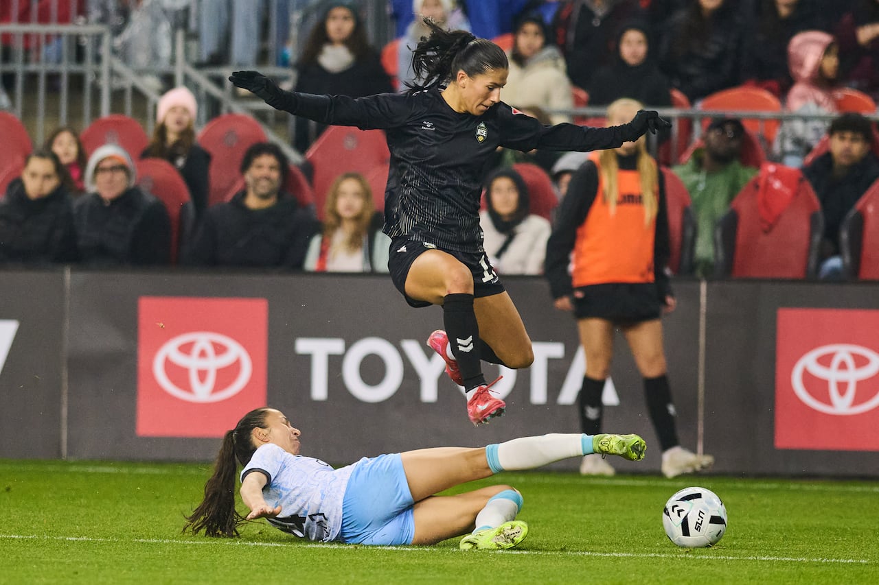 A soccer player representing the Vancouver Rise evades a slide tackle.