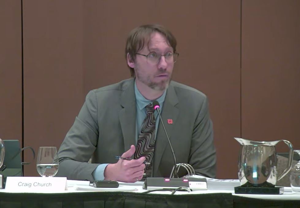 A man in a suit and tie speaks at a microphone.