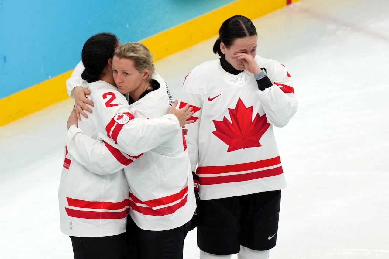 Two hockey players embrace, as another wipes tears from her eyes.