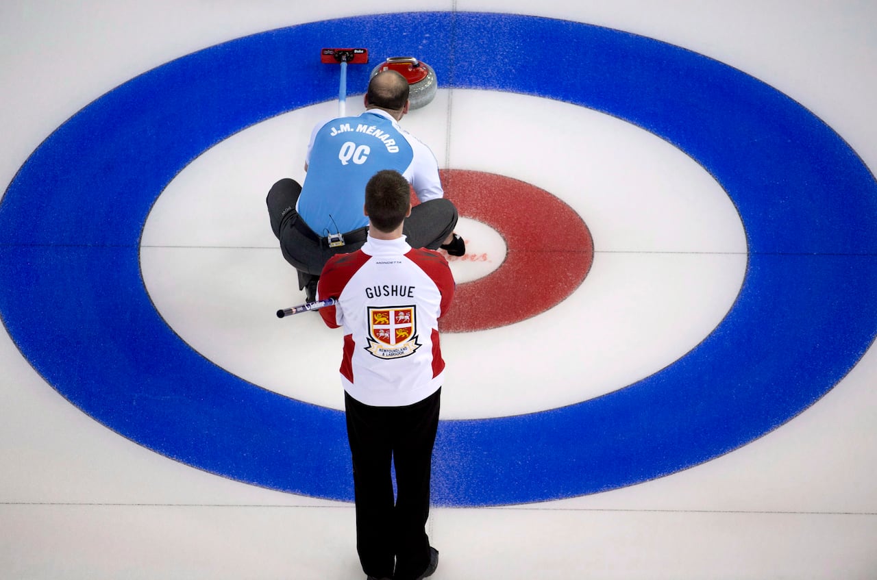 One curler squatting down to line up a shot while the other stands behind him.