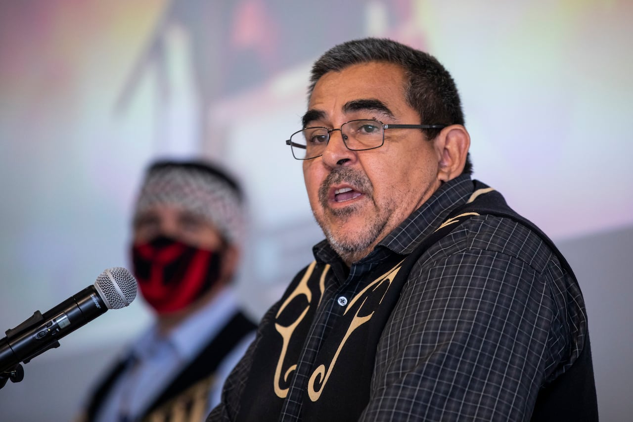 An Indigenous man wearing a checked shirt speaks into a mic.