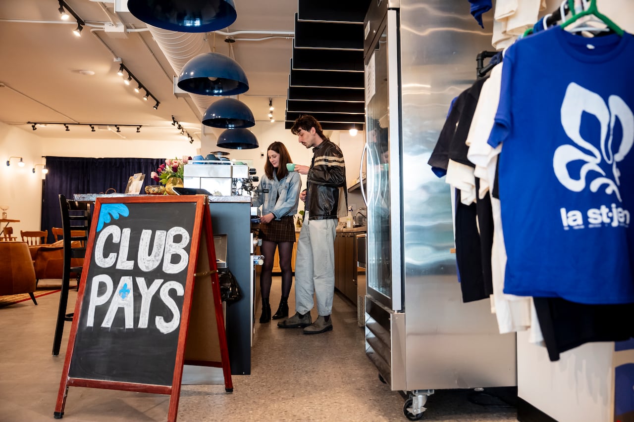 A sandwich board with the words 'Club Pays' is pictured as two people make coffee at a counter in the background.