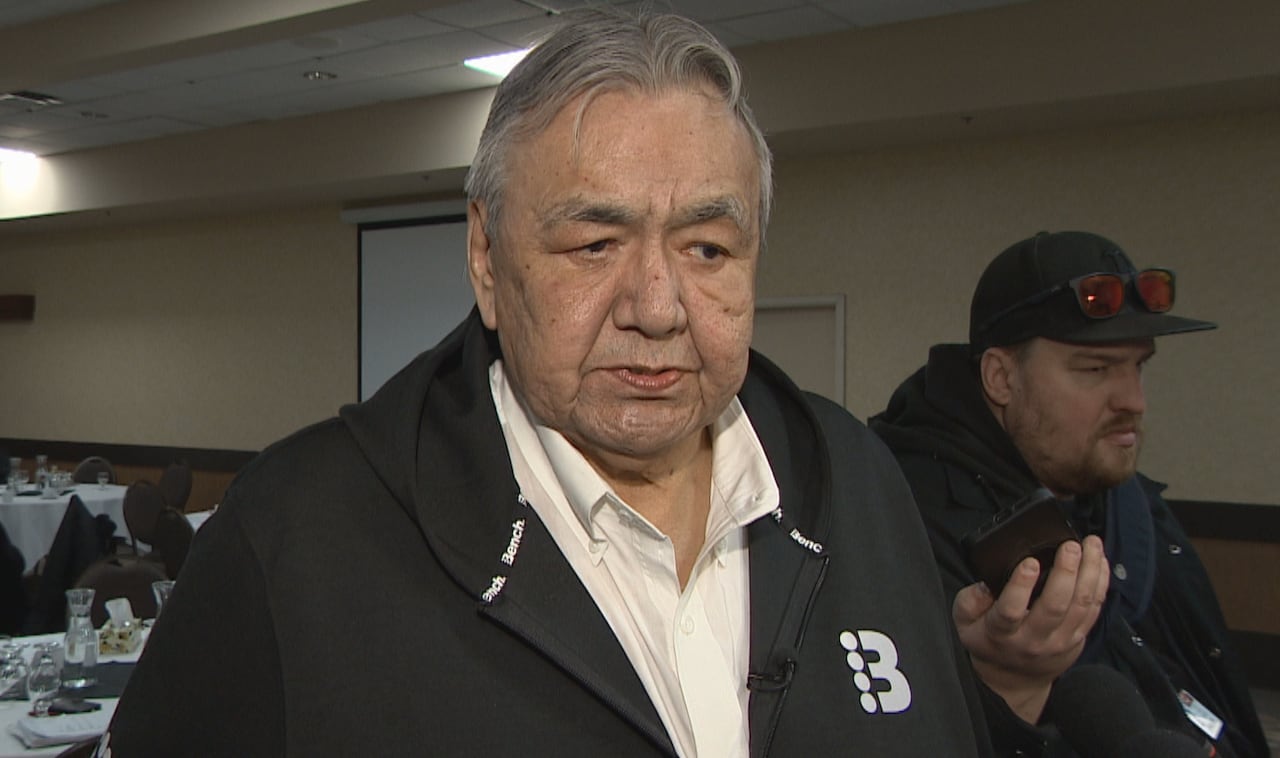 Man with light grey hair wears a black jacket and white button up shirt