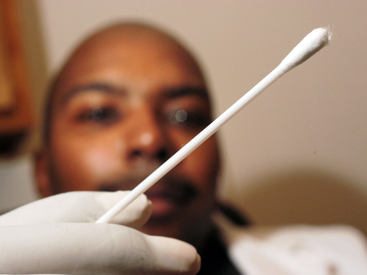 A cotton swab is seen in front of a man taking a DNA test
