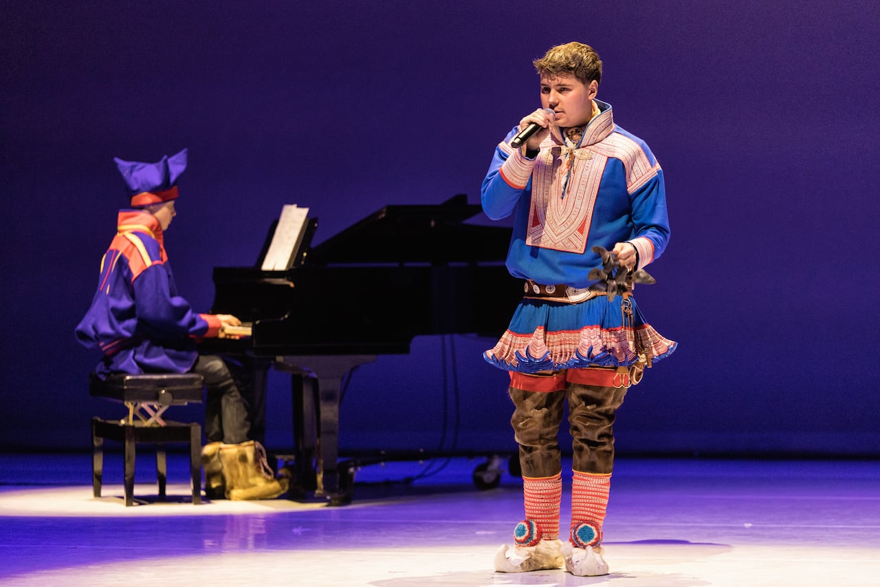 A person sitting at a piano and another person standing and singing