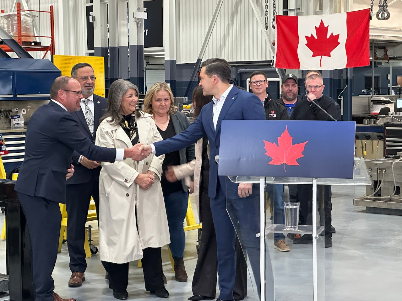 A man in a suit shaking hands with another man in a suit as workers look on 