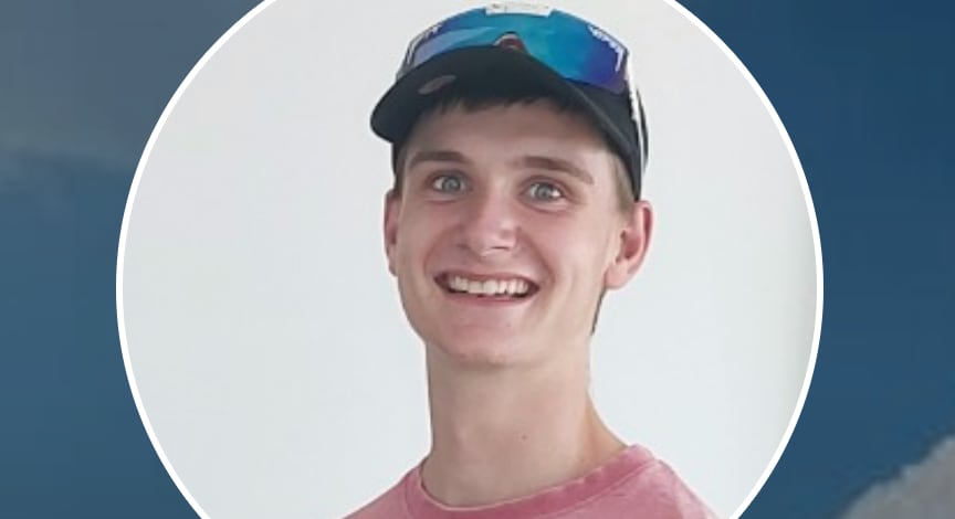 A young man wearing a ball cap, smiles at the camera. 