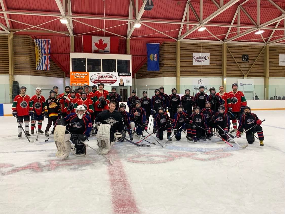 a group of young and old hockey players in red and black jerseys pose for a picture on ice