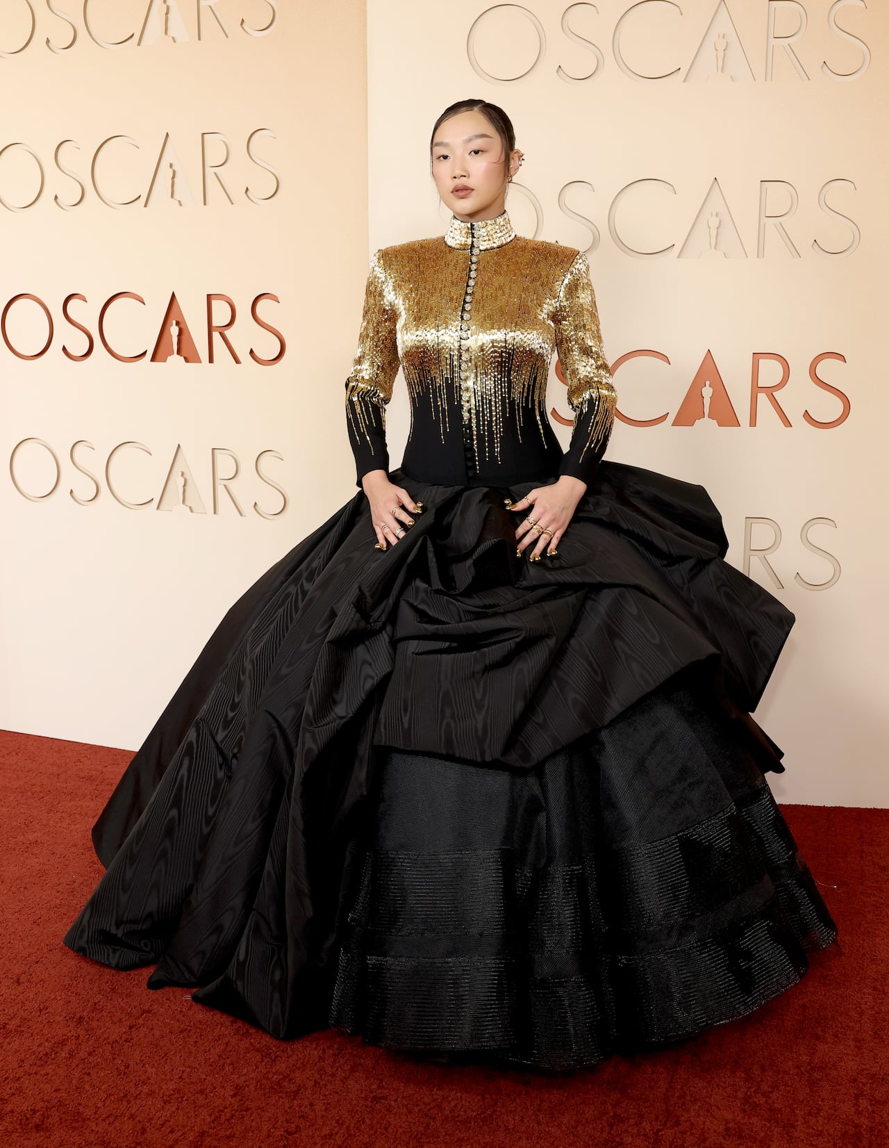 A woman poses for a photo wearing a long-sleeve gown thats gold on top and has a voluminous black skirt. 