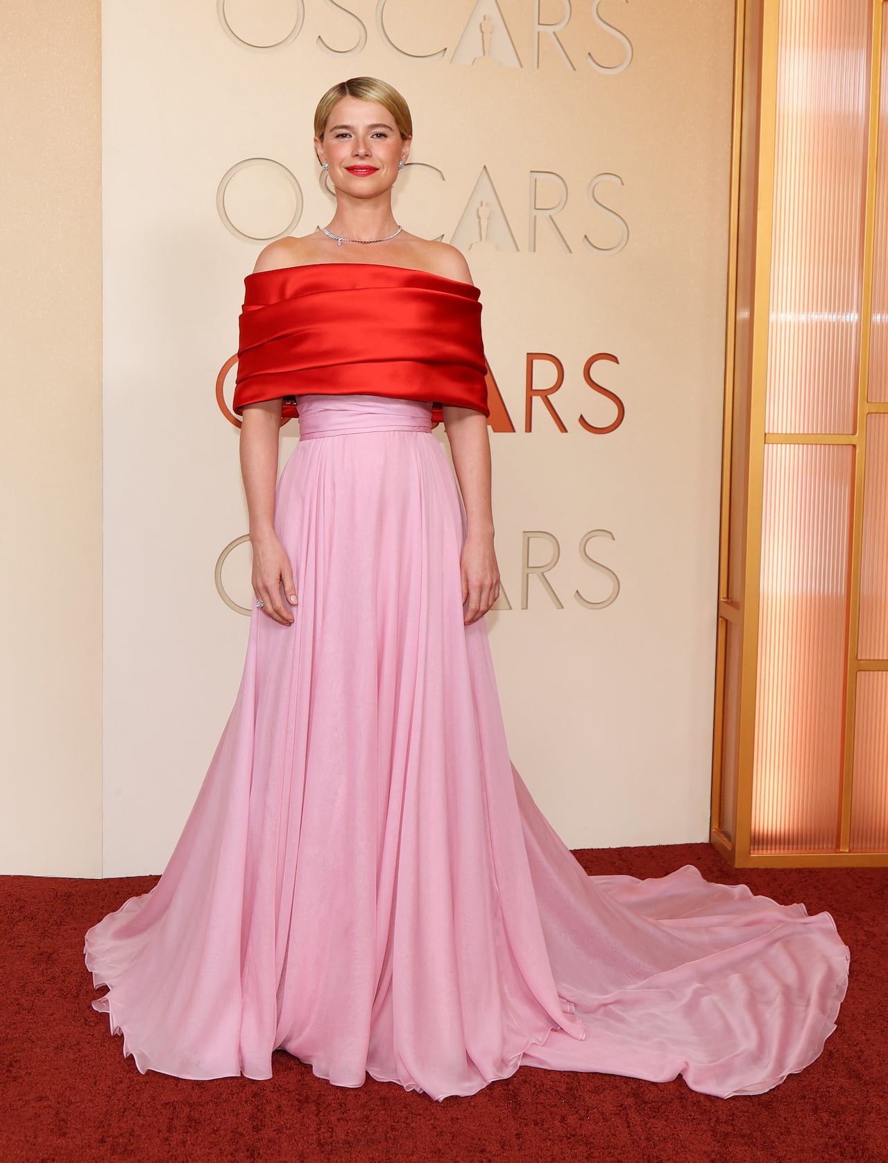 A woman poses for a photo wearing an off-the-shoulder gown that's red on top and pink on the bottom.