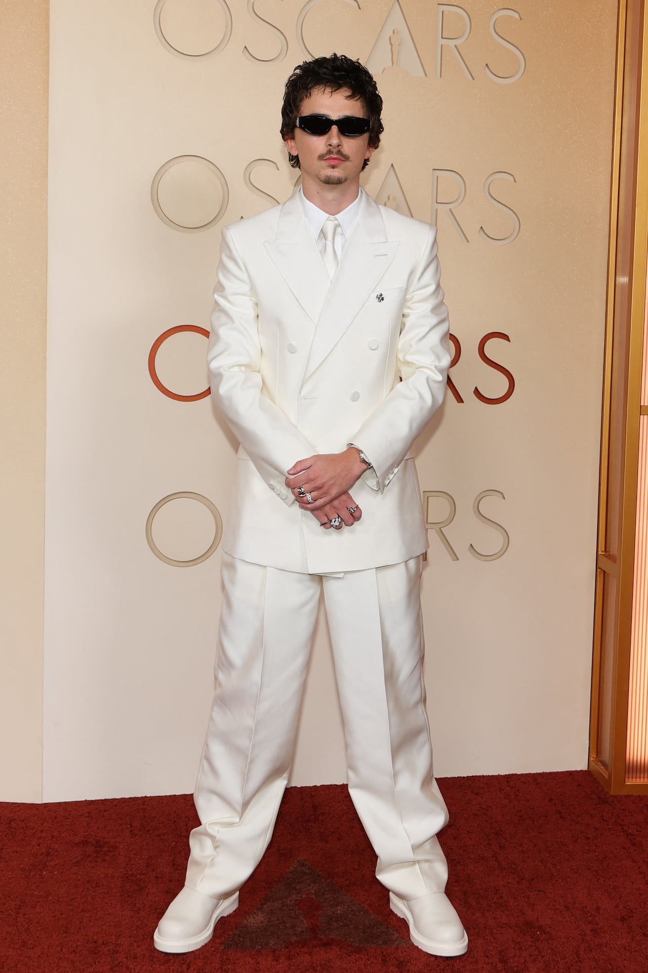 A man poses for a photo wearing a white tux and shoes with black sunglasses.