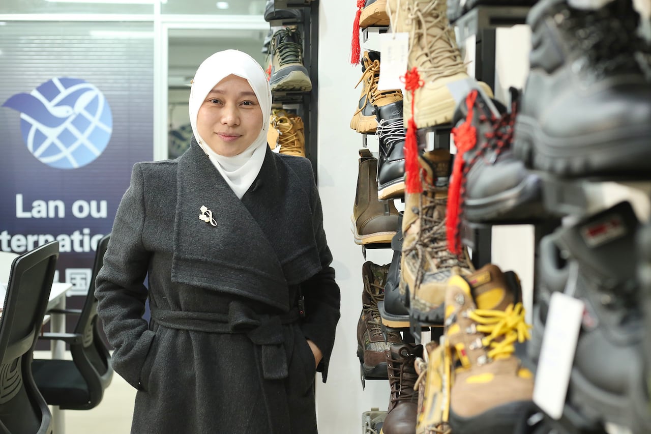 A woman in a headscarf stands next to display shelves with shoes.