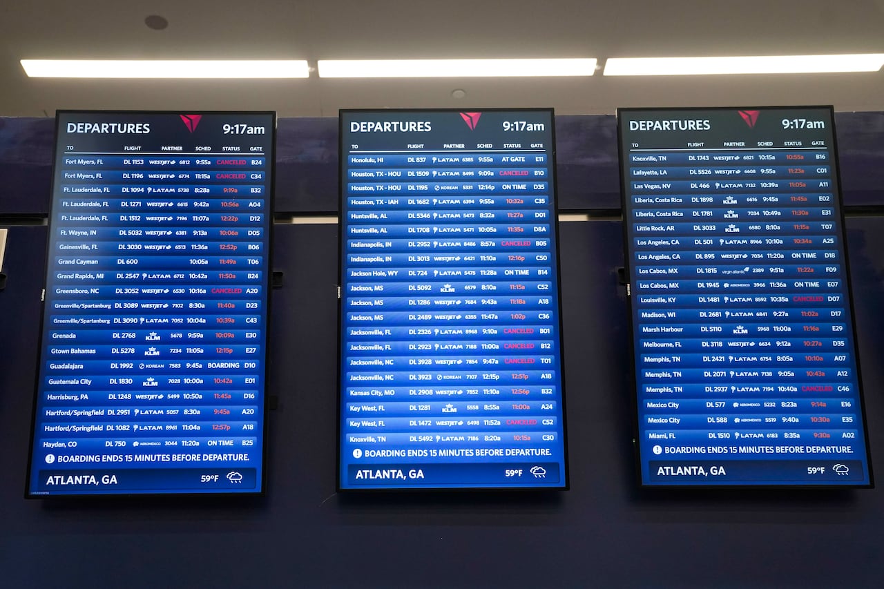 Three vertical monitor screens with several blue lines with white type showing flight departure cancellations and delays.