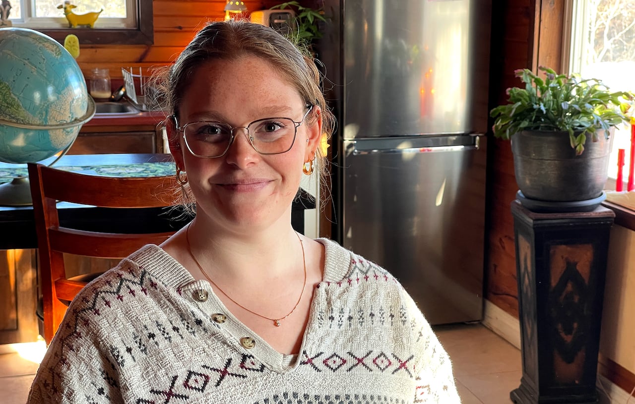 A woman in glasses sits in her kitchen.