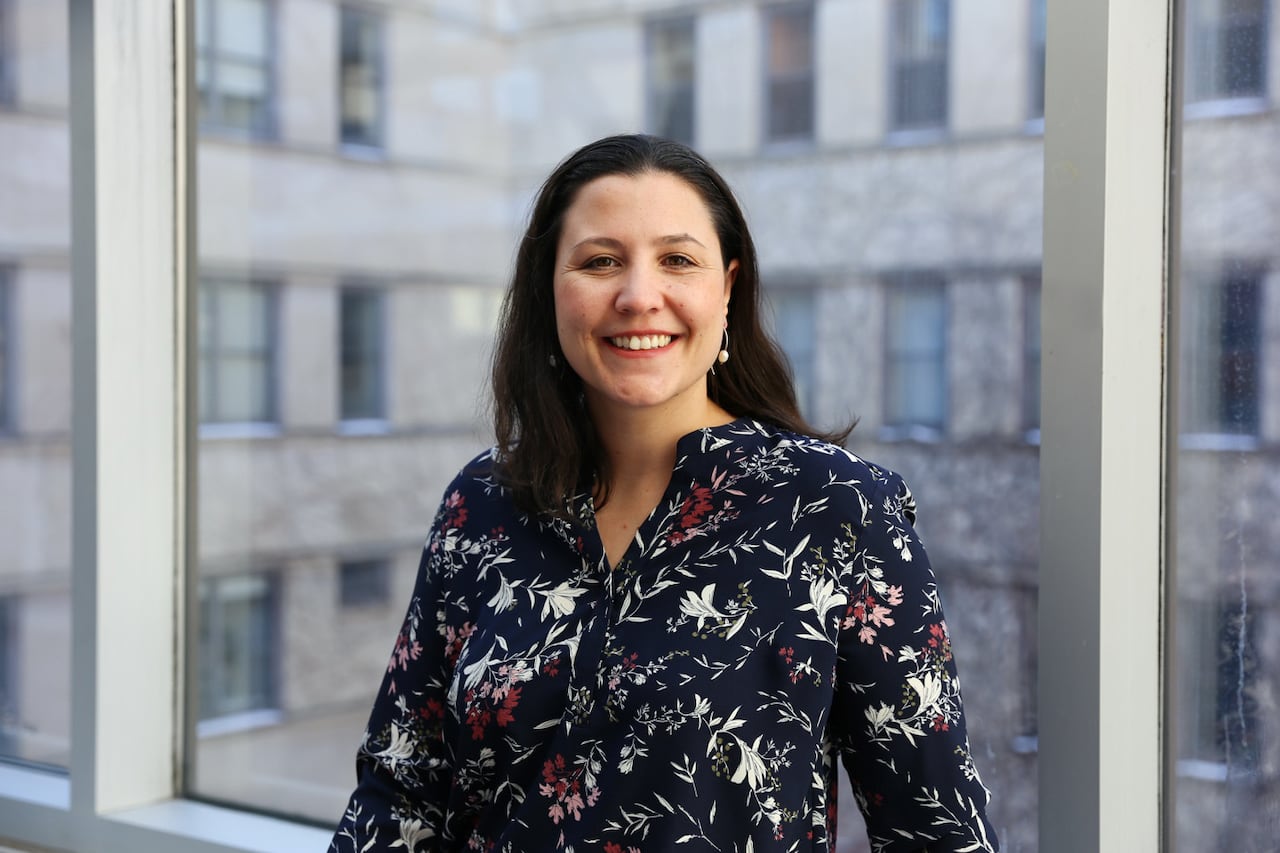 A smiling woman stands in front of a window.