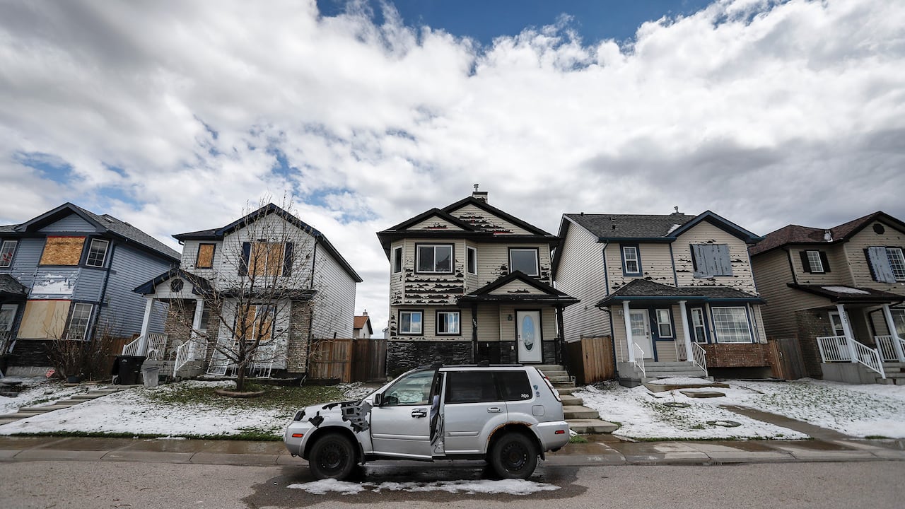 An SUV is parked in front of a series of homes damaged by extreme weather.