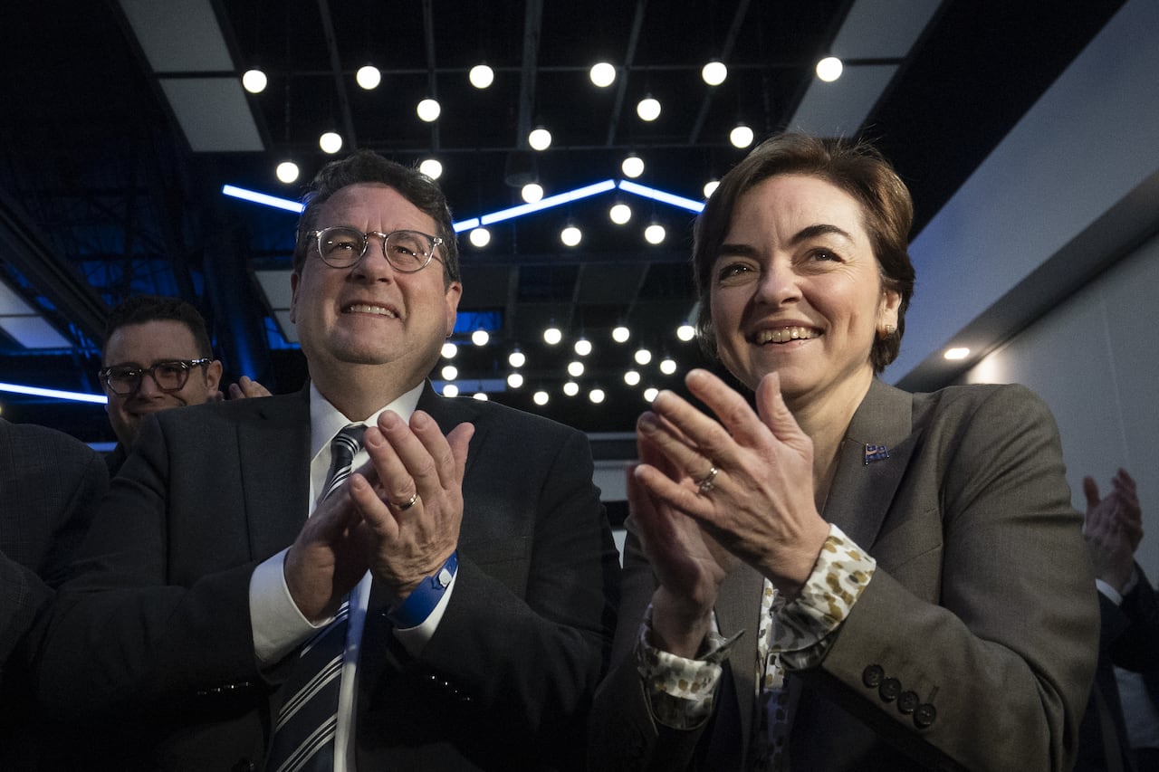 A man in glasses and a woman with short hair applaud.