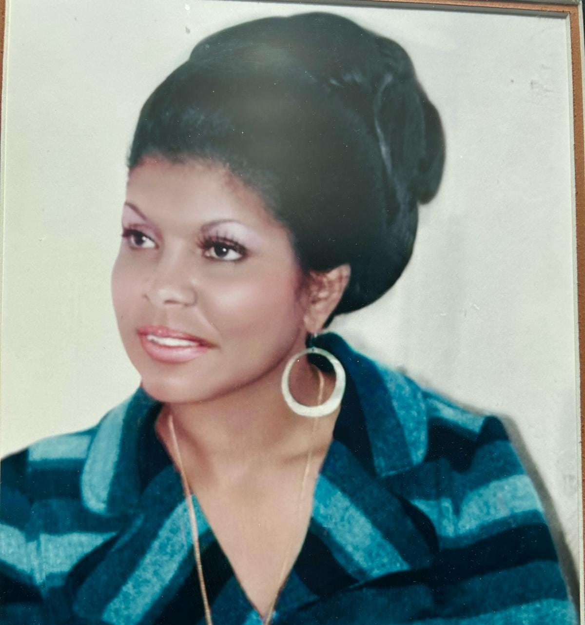 Young woman poses for portrait fashionably dressed with big hoop earrings and perfectly styled hair.
