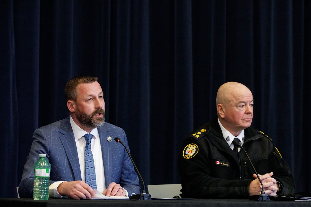Two men speak while seated at a table in front of microphones.