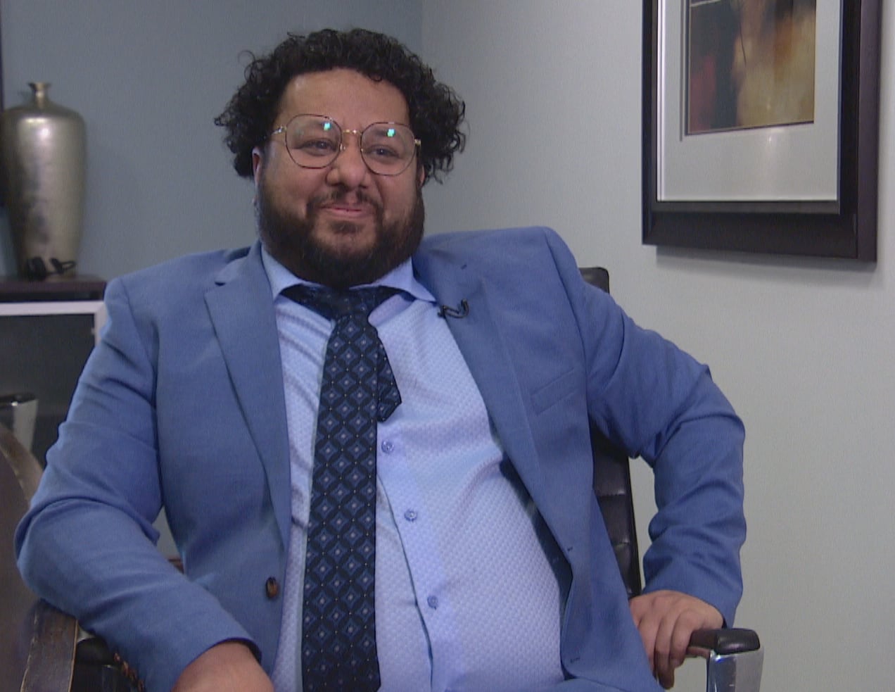 Man with glasses and a suit smiles. 