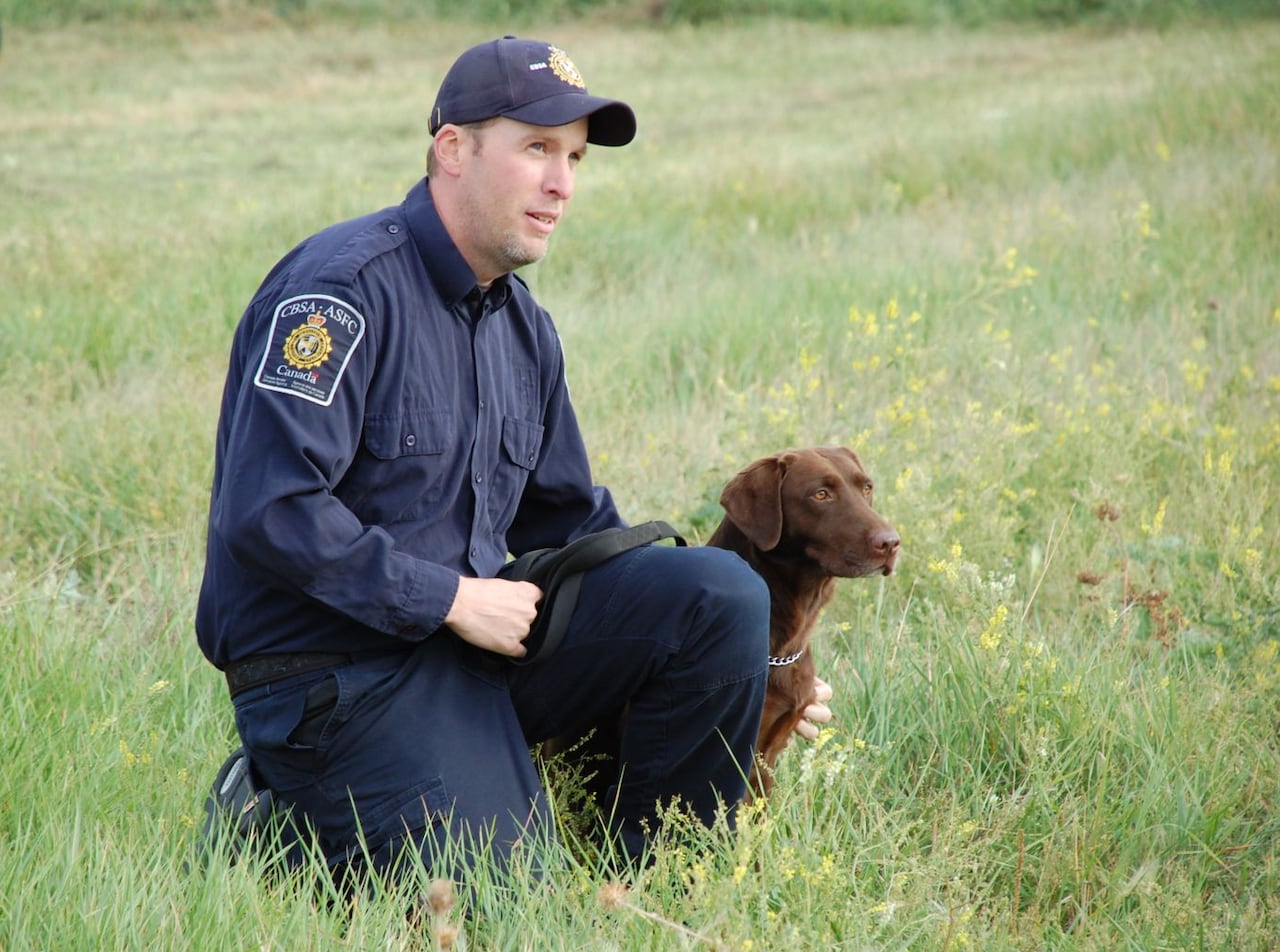 Man in a uniform kneels down beside a dog in a field.