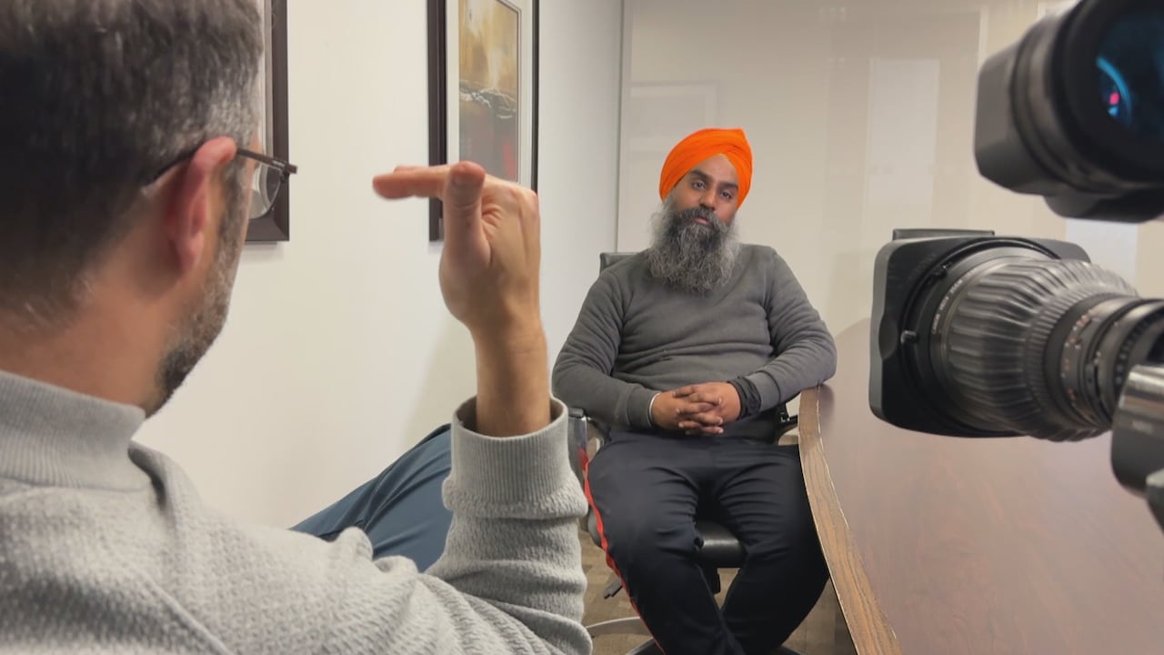 Man in a turban being interviewed by a reporter in a meeting room.