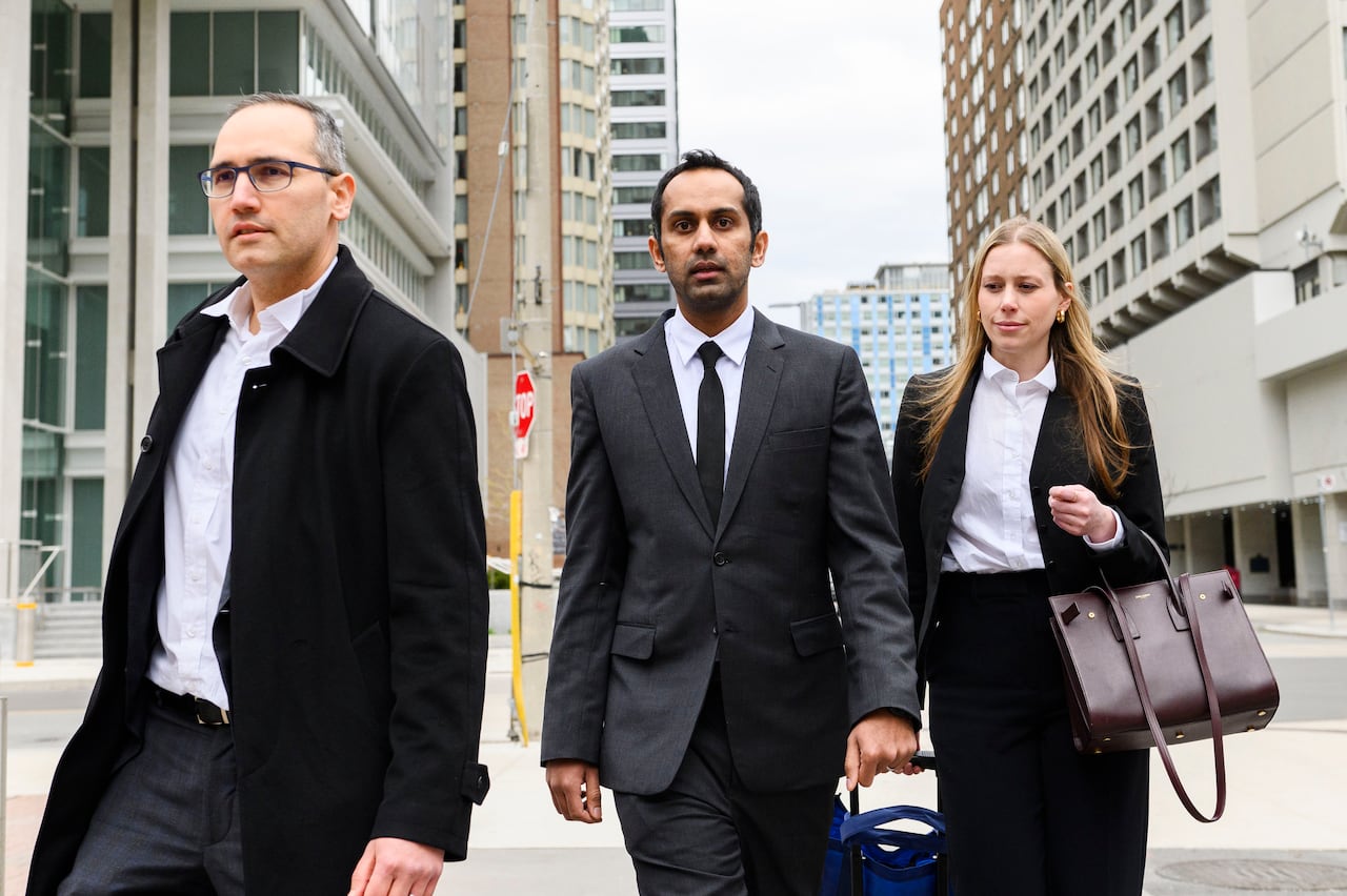 Three people, two men on the left and a woman on the right, walk out of a courthouse in Toronto. 