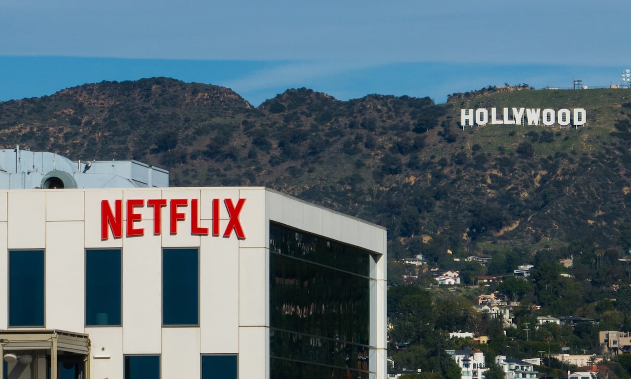 A Netflix sign is displayed atop a building, with the Hollywood sign visible on a hill in the distance.