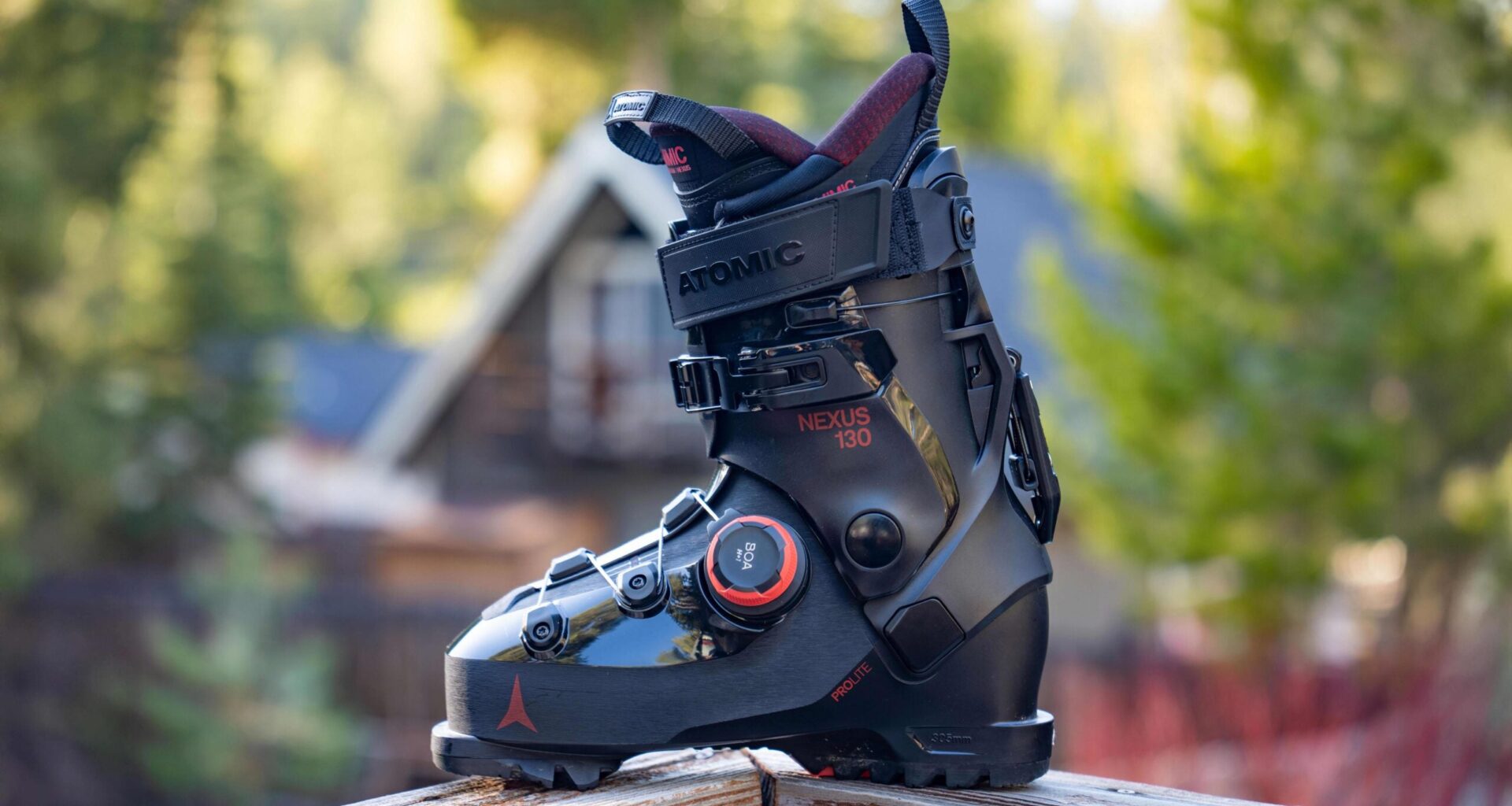 Closeup of black Atomic Nexus 130 BOA ski boot on wooden railing with blurry trees in background