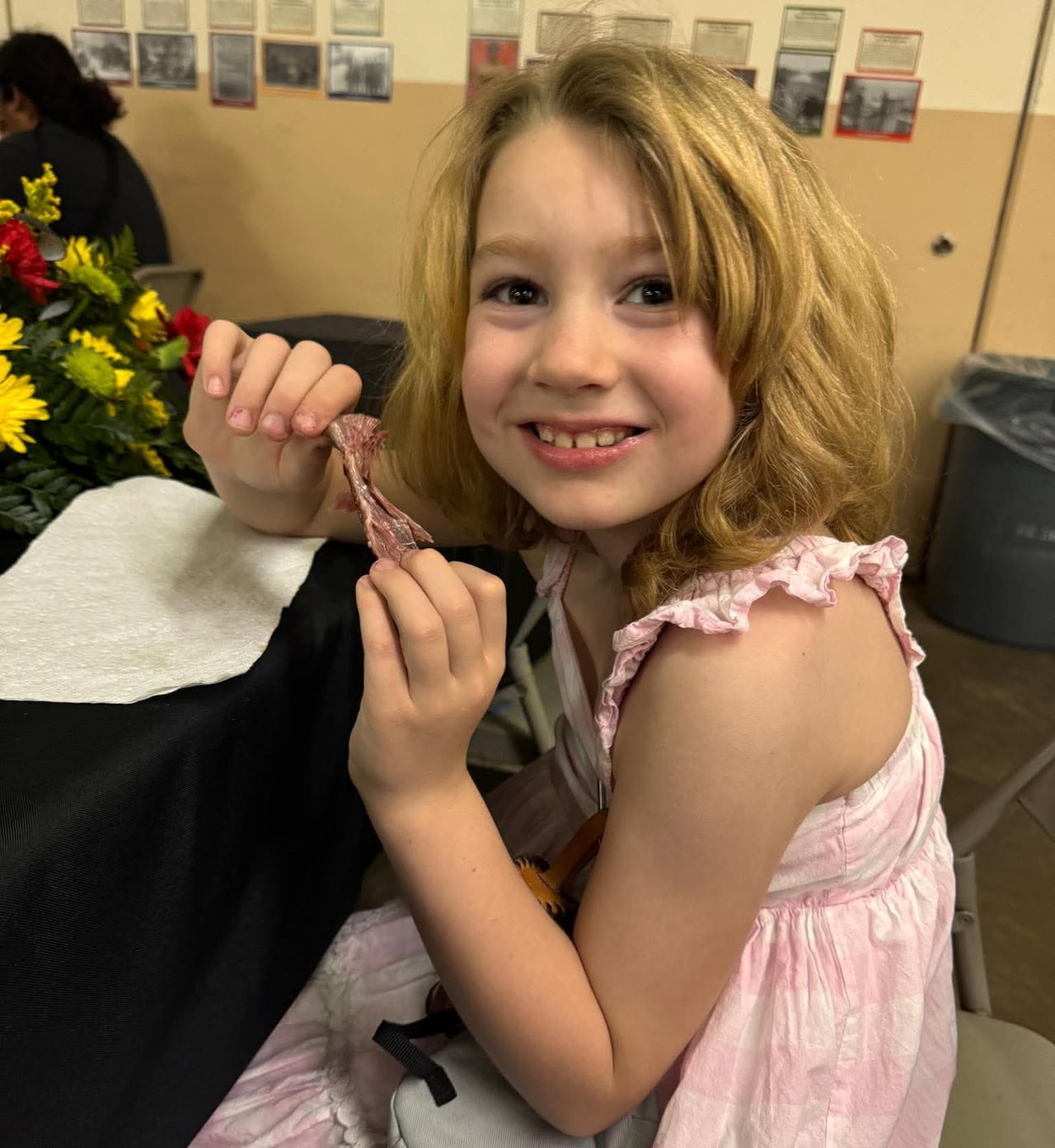 A blond girl smiles while seated at a table.